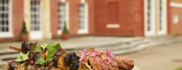 Vegetarian BBQ option on wooden board, held up with Hinxton Hall in the background.