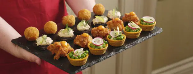 Waitress with a red apron holding plate of canapés