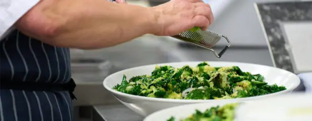 lime zest being grated to broccoli salad