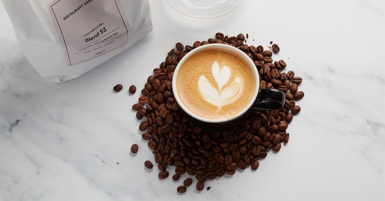 Cup of coffee, surrounded by coffee beans and a white bag saying Blend 53.