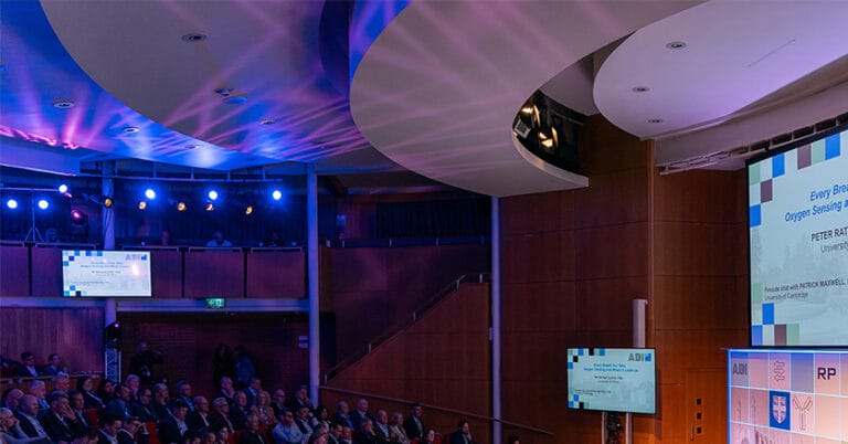 Light fittings projecting blue and pink light with white criss-cross shapes onto ceiling of auditorium.