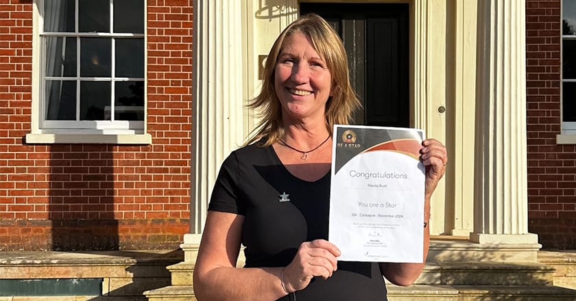 Photo of Hayley Scott standing in the sunshine outside Hinxton Hall holding a piece of paper that's her certificate.