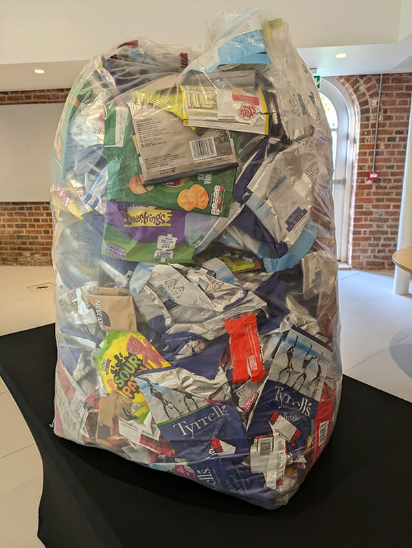 Big transparent bin bag with lots of crisp packets inside.