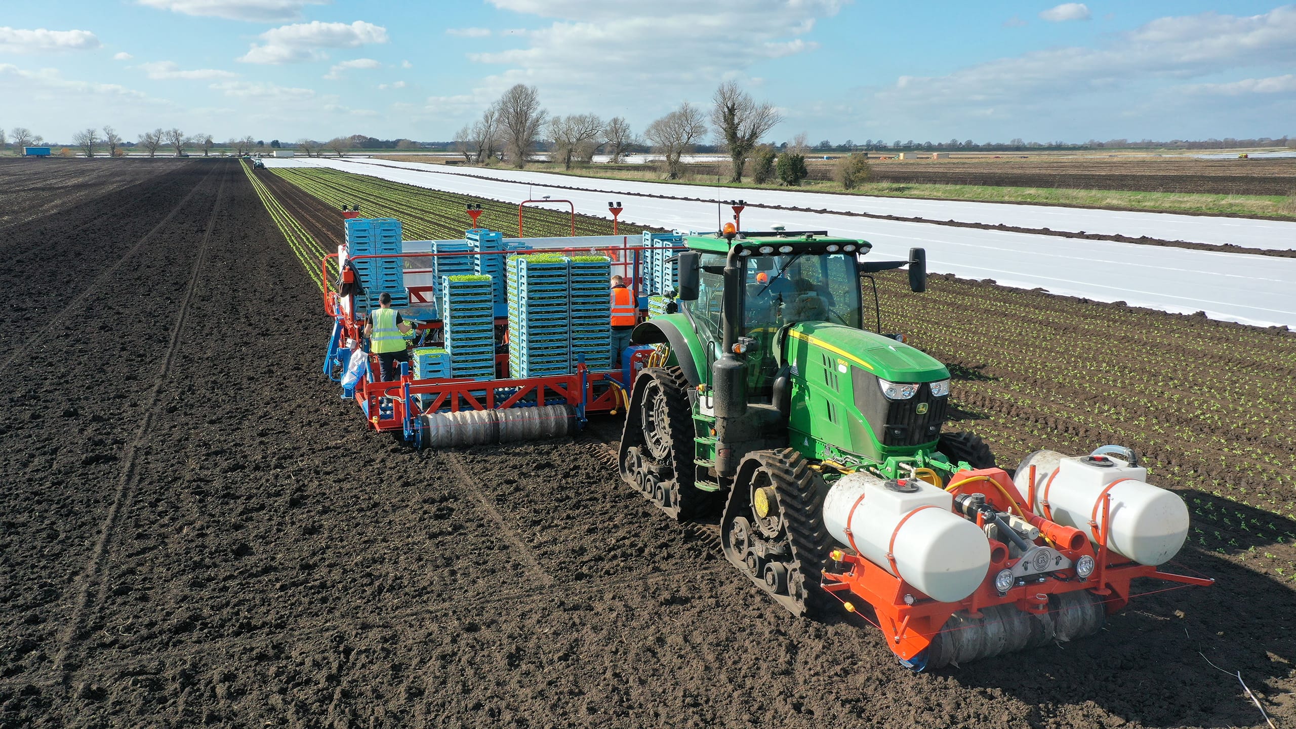 Farming machinery in large field of dark soil.